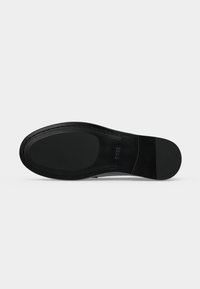 Semelle de chaussure noire avec une surface lisse, forme ovale à l’avant et talon rectangulaire, photographiée par en dessous sur un fond gris clair.