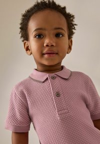 Polo shirt rosa chiaro con un motivo testurizzato, maniche corte, colletto e due bottoni grigi sul davanti.