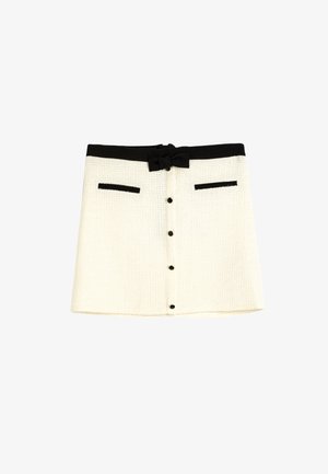 Jupe blanche texturée avec une ceinture en satin noir, deux accents de poche noirs et une fermeture à boutons à l'avant.
