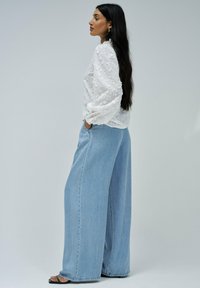 Blusa blanca bordada con mangas abullonadas combinada con jeans de pierna ancha de tiro alto en azul claro y sandalias negras.