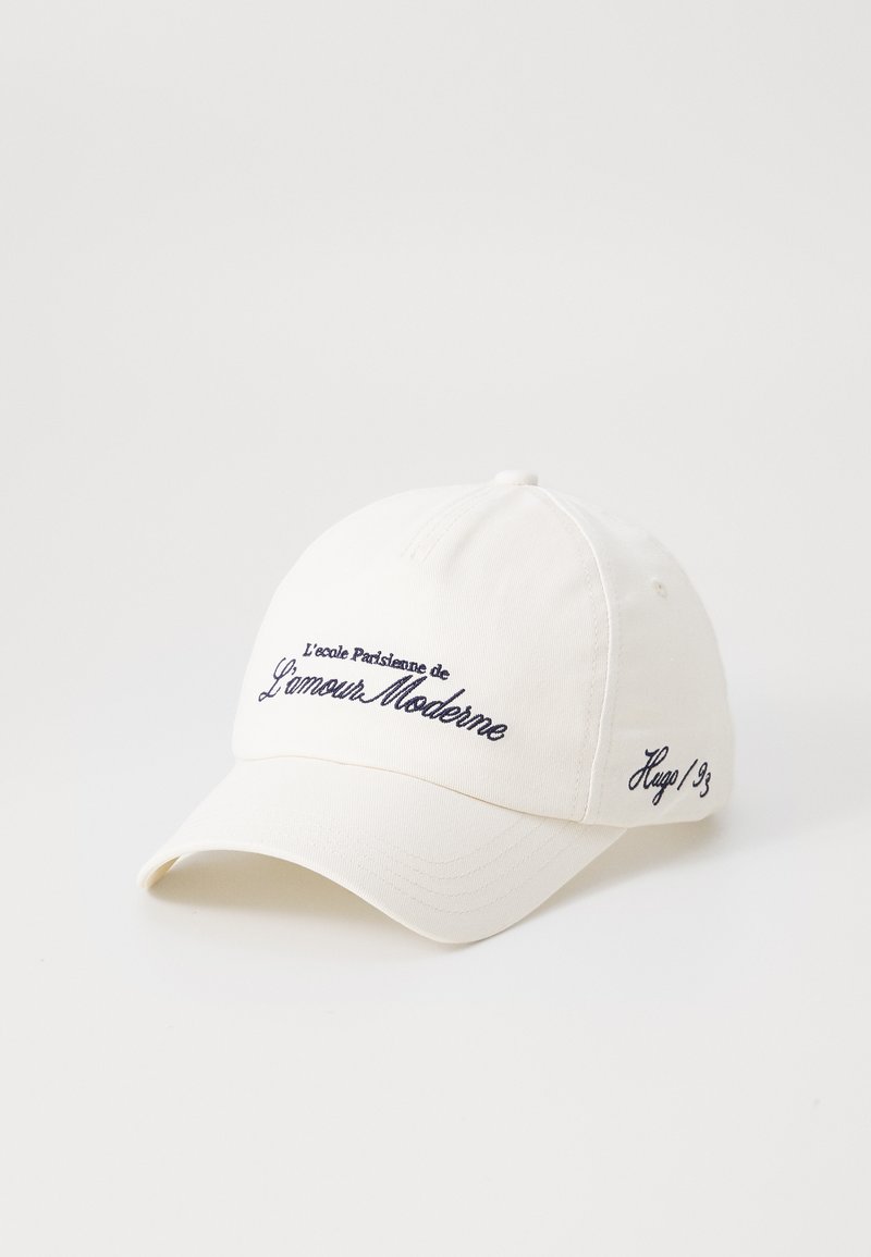 Witte katoenen baseballcap met een gebogen rand. Bevat geborduurde marineblauwe tekst: "L’école Parisienne de l'amour Moderne" en "Hugo/93."