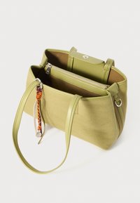 Grüne Canvas-Shopper-Tasche mit einem Reißverschluss-Innenfach, ausgestattet mit einem Druckknopfverschluss und Ledergriffen. Inklusive eines dekorativen Schlüsselanhängers.