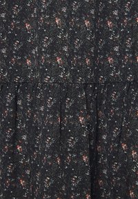 Černé květinové šaty s volánkem. Obsahují malé květy v odstínech červené, bílé a zelené na texturovaném pozadí.