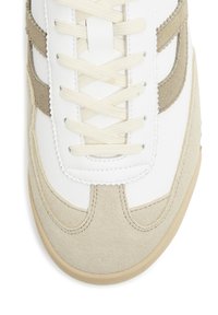 White leather sneakers with beige suede accents, featuring flat beige laces, a rounded toe, and stitching details on the upper.