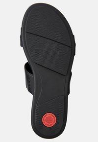 Svart sandalbotten med en strukturerad halkskyddsyta, böjd form och röd cirkulär logotyp med texten "KOMFORT. TEKNIK. FITFLOP."