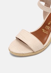 Sandale en cuir beige avec une texture crocodile, dotée d'une large sangle et d'une semelle de style espadrille. Doublure intérieure marron et détail de marquage doré.