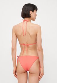 Korálový bikiny set so zaväzovaním okolo krku, spodná časť s minimálnym pokrytím a hladkým, elastickým materiálom.