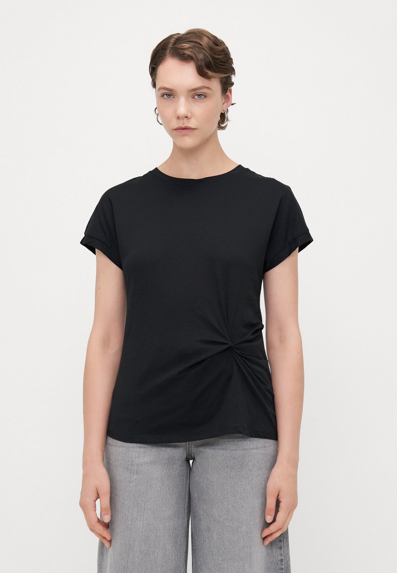 Svart t-shirt med kort ärm, tillverkad i mjukt tyg, med en vriden knutdetalj på framsidan och en avslappnad passform.