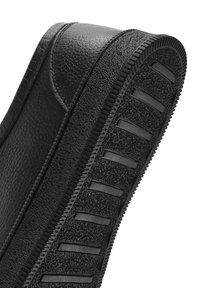 Ceinture en cuir noir texturé avec dessous en caoutchouc rainuré conçue pour l'adhérence et la durabilité, courbée pour montrer les détails du cuir et de la semelle.