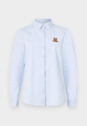 Lyseblå langermet skjorte med knapper, hvite vertikale striper og en brodert teddybjørn på venstre bryst. Laget av bomull.