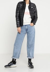 Sort puffjakke med blank finish, grå sweatshirt med logo, lyseblå baggy jeans og sorte sportssko med hvide accenter.