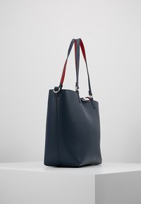 Granatowa skórzana torba typu tote z czerwono-niebieskimi paskami, prostokątny kształt, gładka tekstura, metalowe detale i minimalistyczny design.