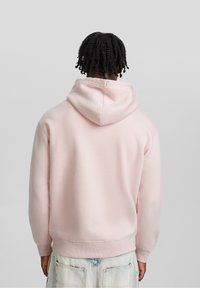 Felpa con cappuccio in cotone rosa con cappuccio spazioso, polsini e orlo a costine; vista posteriore che mostra una texture liscia e un design minimalista.