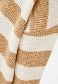 Zbliżenie na miękką dzianinę z szerokimi poziomymi paskami w odcieniach beżu i bieli.