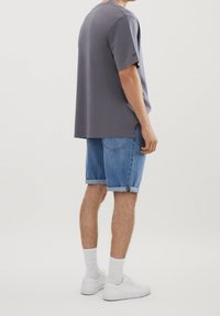 Camiseta de algodón gris de corte relajado, combinada con shorts de denim remangados. Zapatillas blancas y calcetines hasta los tobillos completan el conjunto.