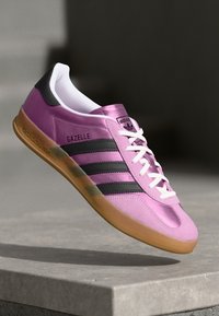 Pink syntetisk overdel med tre sorte striber, hvide snørebånd og en gummisål. Har "Gazelle" branding på siden. Low-top design.