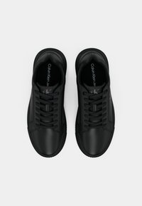 Zapatillas de cuero negro con punta redonda, suela plana de goma y diseño de cordones. Presenta un branding mínimo en la plantilla. Textura suave.
