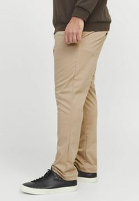 Krémové kalhoty ze směsi bavlny se slim fit střihem, s hladkým povrchem a minimálními švy, doplněné o černé tenisky.