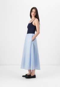 Top sin mangas de color azul marino combinado con una falda midi a rayas azules con bolsillos, acompañado de zapatos planos negros para un look casual.