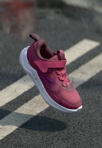 Nike-sneaker i mörkrosa med mesh-överkänslan, vadderad krage, justerbar rem och vit sula; har lila detaljer och texturerade inslag.