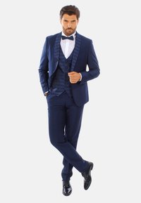 Tuxedo navy con rever a motivo, camicia bianca e papillon. Fit su misura, abbinato a scarpe lucide nere e pantaloni slim.