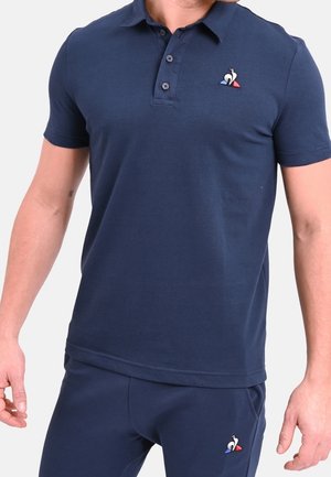 Dunkelblaues Polohemd aus weicher Baumwolle mit einer Knopfleiste mit drei Knöpfen und gesticktem Logo auf der Brust. Kurze Ärmel und eine taillierte Passform.