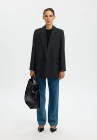 Temno sivi dvoredni blazer z ožjim krojem in teksturirano tkanino. Kombiniran z modrimi kavbojkami z visokim pasom in veliko črno usnjeno torbo.