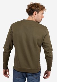 Sudadera verde oliva con cuello redondo, mangas largas y puños y dobladillo acanalados. Textura suave y ajuste medio.