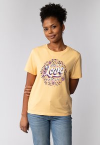 T-shirt en coton jaune avec un col rond, présentant un motif floral imprimé et le texte "SEULEMENT L'AMOUR AUJOURD'HUI" en violet et blanc.