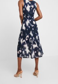 Abito senza maniche a linea ad A in blu navy con design astratto bianco. Tessuto morbido, lunghezza a metà polpaccio e una leggera apertura sul retro. Indossato con tacchi neutri.