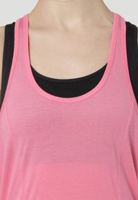 Różowy sportowy top na ramiączkach z okrągłym dekoltem. Nałożony na czarny top, charakteryzuje się gładką fakturą i kontrastującymi ramiączkami.