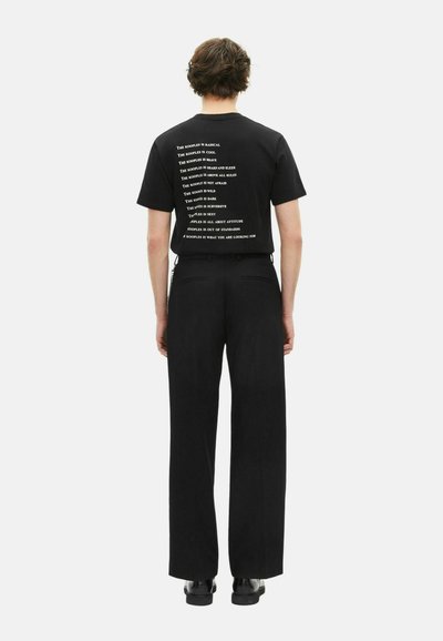 Camiseta negra con texto blanco en la parte posterior, que presenta diversas frases. Combinada con pantalones negros holgados y zapatos negros.