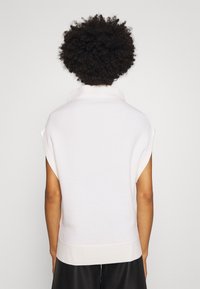 Weißes ärmelloses Oberteil mit hohem Kragen, weicher Textur und lässiger Passform. Rippdetails am Saum unterstreichen die minimalistische Ästhetik des Designs.