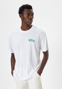 Hvid bomulds t-shirt med et grønt grafisk print med ordet "UNBELIEVABLE." T-shirten har korte ærmer og en rund halsudskæring.
