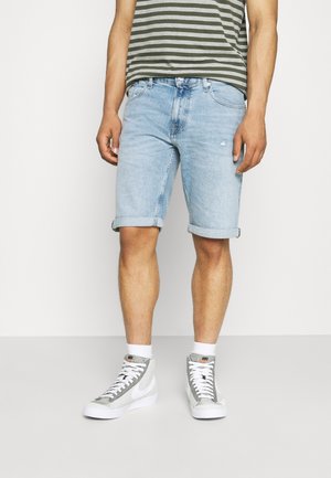Hellblaue Jeansshorts mit umgeschlagenen Säumen, kombiniert mit einem grauen und grünen gestreiften T-Shirt und grauen High-Top-Sneakern.