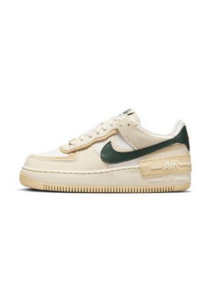 Beżowy sneaker niskiego profilu z zielonym logo Nike, beżową podeszwą, warstwowym skórzanym wzorem oraz "AIR" wytłoczonym na pasku z tyłu buta.