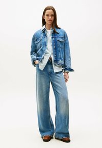 Giacca di jeans con due tasche sul petto, blu chiaro, vestibilità comoda. Abbinata a jeans a gamba larga blu chiaro e una camicia a righe sotto.