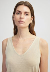 Top sin mangas color beige con diseño de escote en V. Fabricado en una tela suave y ligera. Textura lisa con un sutil brillo.