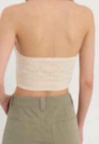 Haut court en maille couleur crème ; motif texturé avec ourlet côtelé. Associé à un pantalon taille haute vert olive, mettant en valeur la taille.