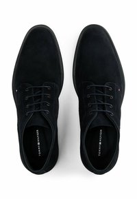 Un paio di scarpe da uomo in pelle scamosciata nera con lacci viste dall'alto su sfondo bianco.