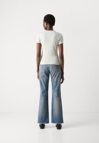 Gestreept lichtgroen short-sleeve topje gecombineerd met uitlopende blauwe jeans, die een aansluitende silhouet en subtiele textuur tonen. Gladde, casual uitstraling.