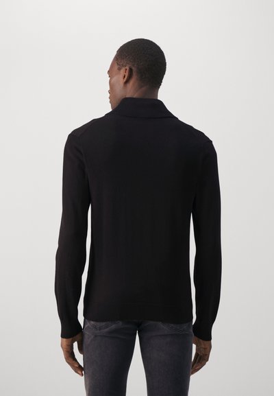Black knit sweater with a collar, long sleeves, and ribbed cuffs. Smooth texture and fitted design, view from the back.