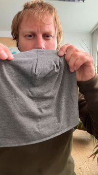 Felpa grigia in tessuto, con una texture liscia e un design con schiena arricciata. Le mani tenute ai bordi mostrano la forma e i dettagli del capo.