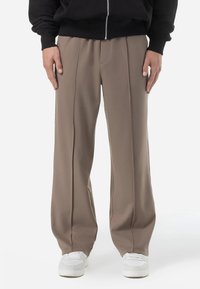 Avslappnade beige byxor med en slät textur, med rak benform och veck fram, i kombination med vita sneakers.