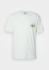 Ljusgrön bomullströja med kort ärm, som har en liten rund grafisk design av gräs och ett ägg på vänster bröstområde.