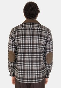 Camicia a quadri marrone, nera e bianca con colletto in velluto a coste e toppe sui gomiti. Maniche lunghe e polsini con bottone. Tessuto testurizzato.