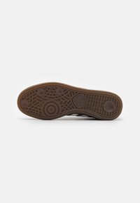 Ruskea kumipohja, jossa on teksturoituja kuvioita, kuten ympyröitä ja viivoja; sisältää Adidas-brändin kolmion muotoisessa logossa.