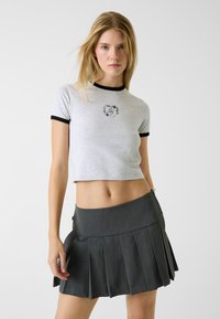 Szary krótki t-shirt z czarnym kołnierzem typu ringer, z motywem kwiatowego logo. W połączeniu z plisowaną mini spódnicą w ciemnoszarym kolorze.