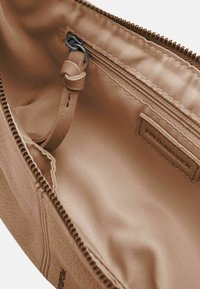 Funda de tela beige con cierre de cremallera, que presenta un interior suave y una etiqueta cosida en el lateral. Detalles exteriores texturizados visibles.