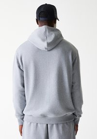 Grå sweatshirt med hætte, lavet af blødt stof. Har en afslappet pasform og ribbede manchetter, parret med matchende grå shorts.